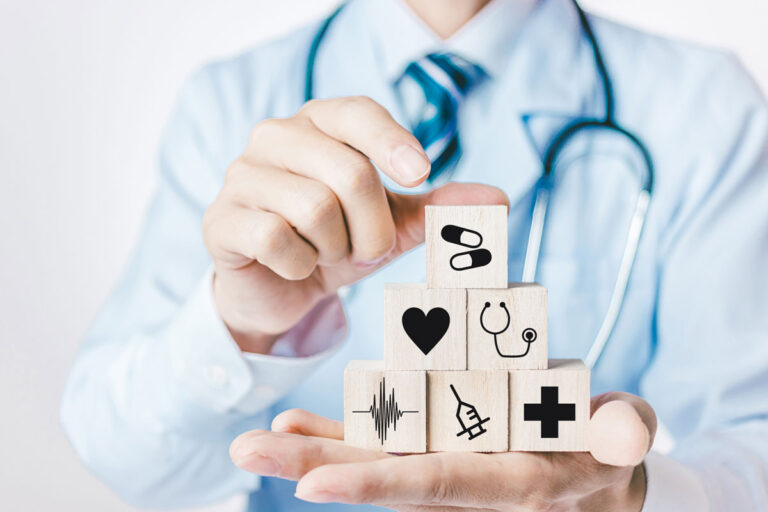 Healthcare professional stacks wooden blocks with medical symbols (heart, stethoscope, syringe, cross) to symbolize health services.