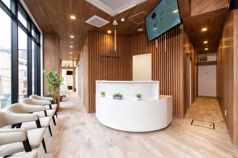 Modern office reception with a curved white desk, vertical wood slats, and beige chairs along a wall of windows.