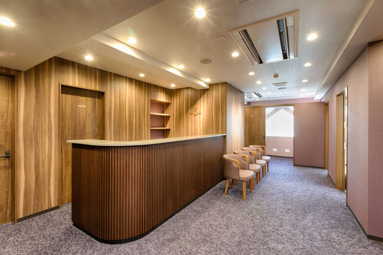 Wood-paneled reception counter with a curved front, beige visitor chairs, and warm ceiling lighting in a corporate lobby.