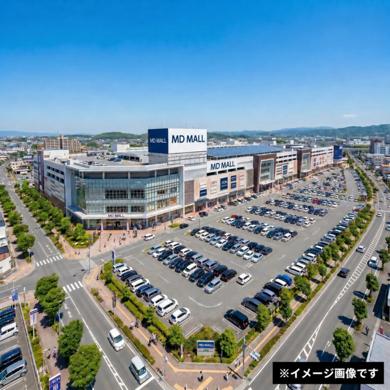 Aerial view of MD Mall complex with glass storefronts, large parking lot, and surrounding roads under a blue sky.